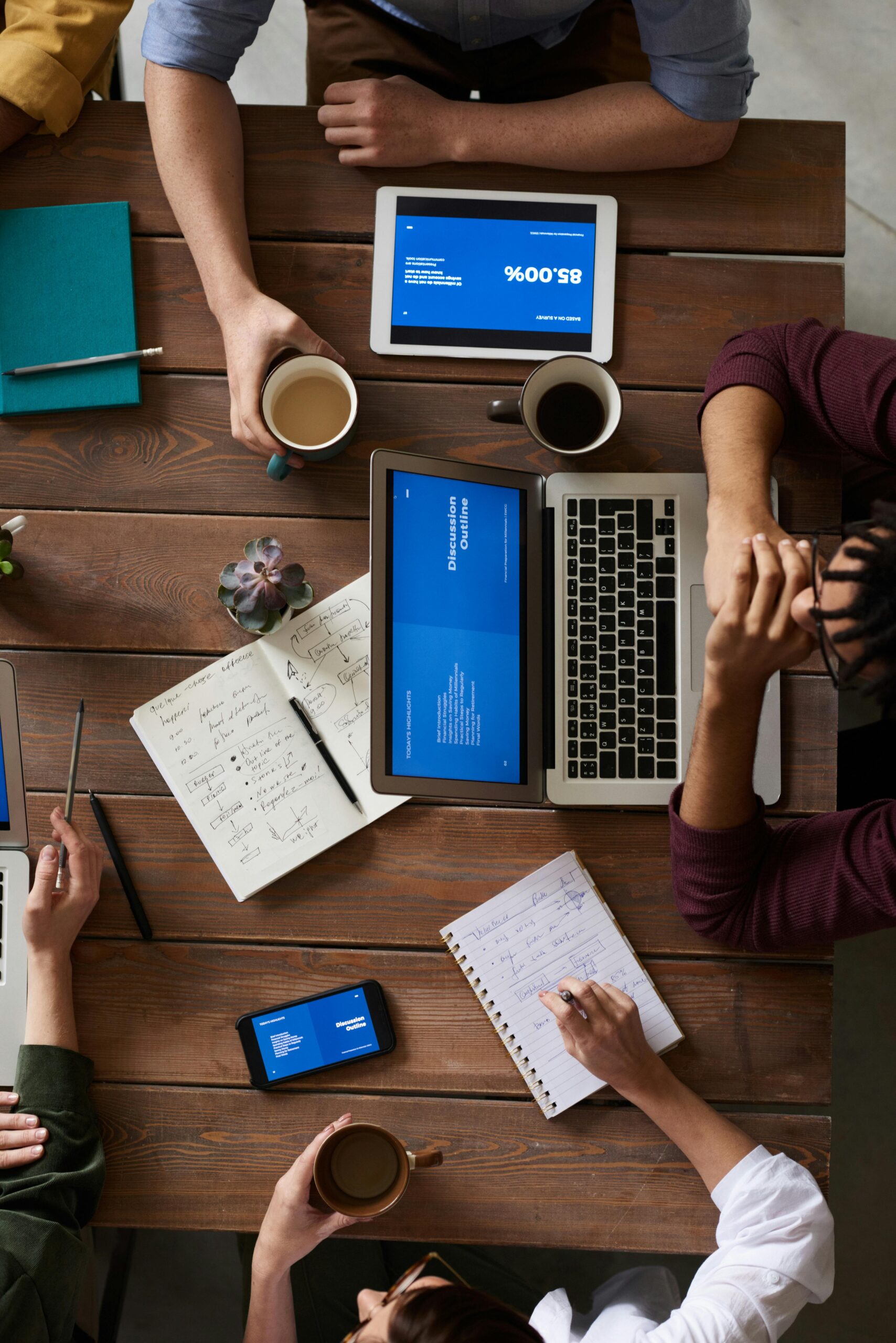 Overhead view of a business team working with laptops, tablets, and notebooks around a wooden table